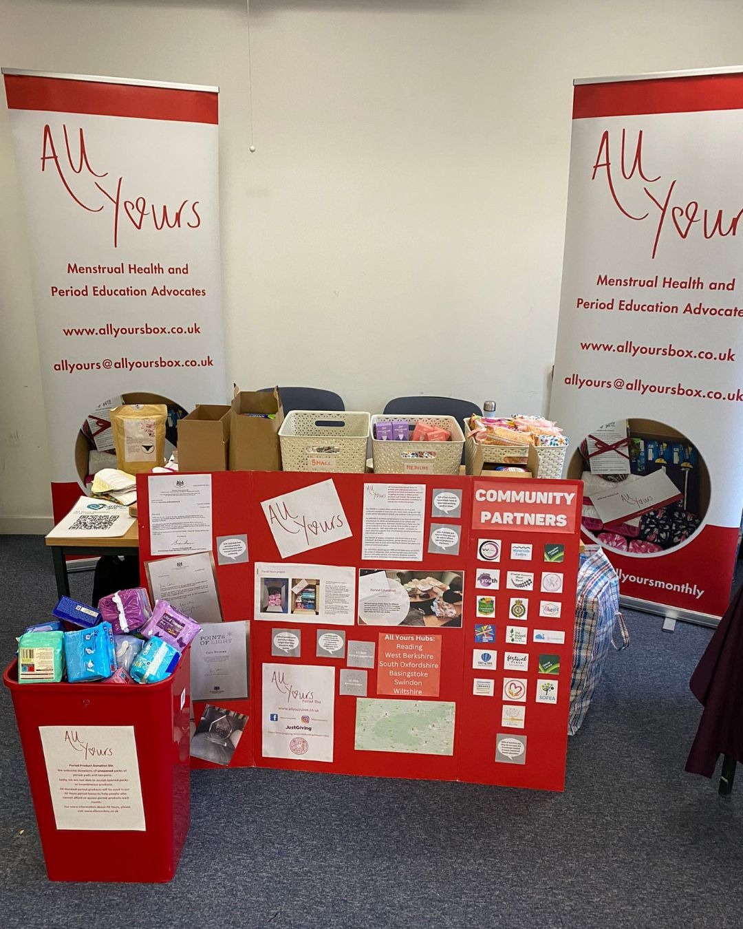 The All Yours Period Box information stand at a community event, with branded banners and a community partners board.